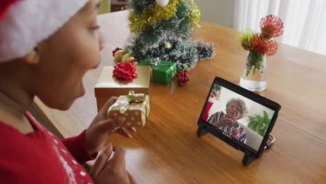 Mujer-Afroamericana-Con-Gorro-De-Papá-Noel-Usando-Tableta-Para-Videollamada-Navideña,-Con-Mujer-En-Pantalla