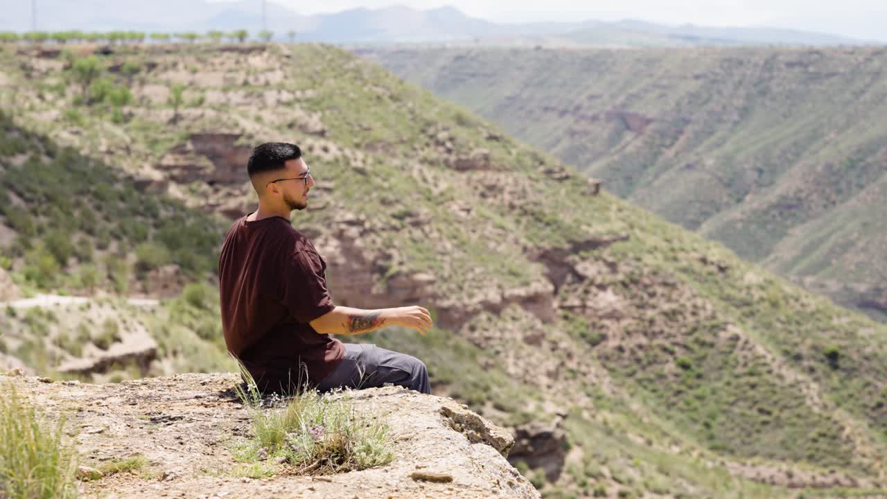 Cheerful male hiker raising arms while sitting on cliff edge