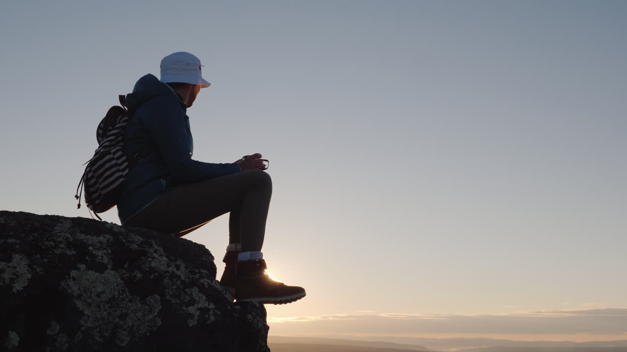un viajero bebe té de una taza en la cima de la montaña se sienta en una roca en el fondo un rojo