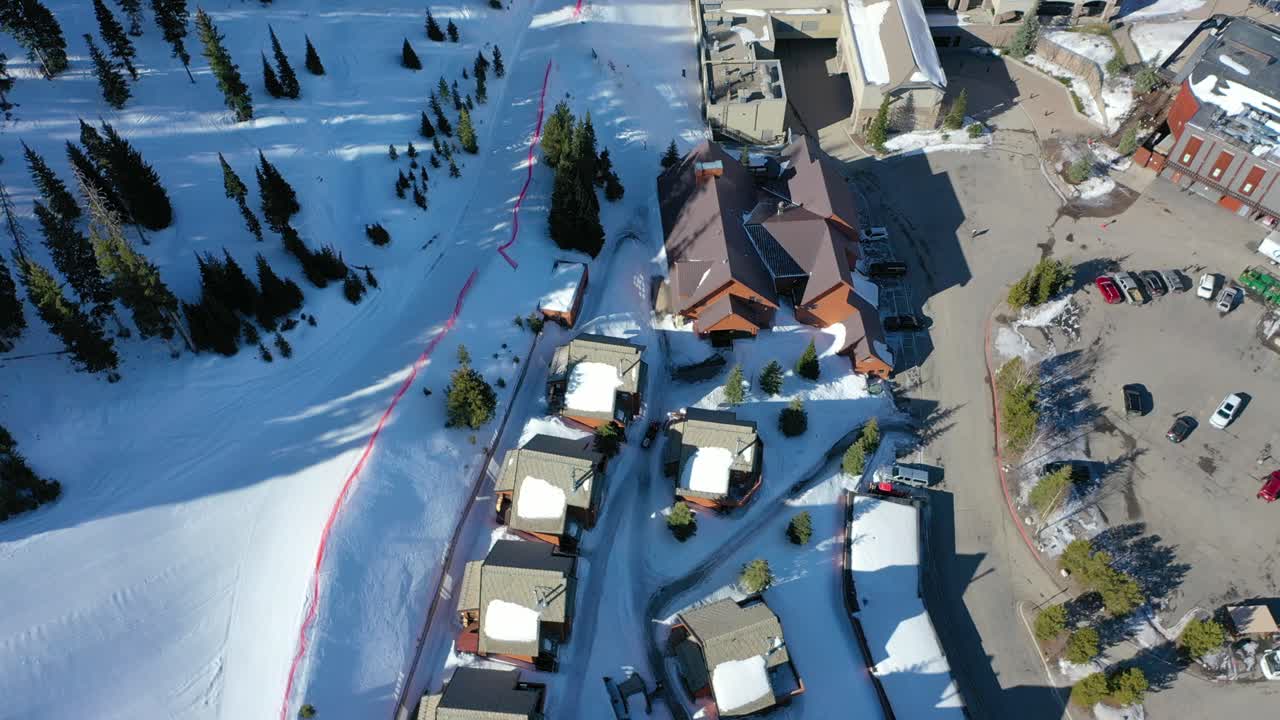 Bird’s eye drone view of a snowy mountain chair lift carrying skiers above powdery slopes and pine-lined trails, surrounded by scenic winter peaks in a peaceful alpine landscape