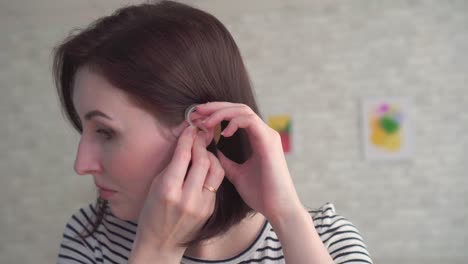 hard of hearing young woman inserts a hearing aid into her ear