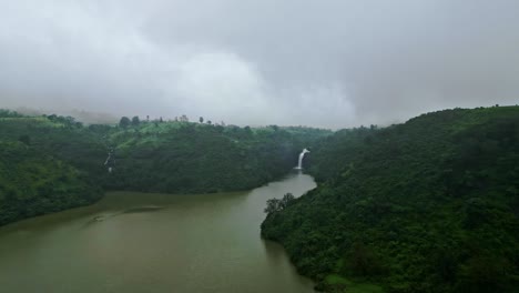 a stunning aerial view of bhandardara, maharashtra, india showcasing its serene lake and majestic waterfalls amid lush greenery. the cloudy sky casts a mystical charm 4k