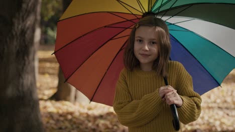 portrait of caucasian girl in the park holding a colorful umbrella.