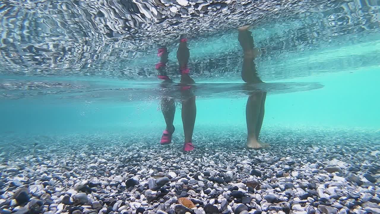 Legs of people walking under cold crystal water of mountain river over pebbles creating air bubbles