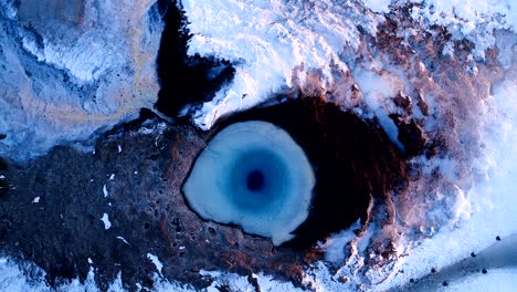 wonderful aerial view of a drone which getting further and further of the center of a geuser in geysir, iceland . smoke is getting out of the geyser with people walking all around the geyser, under the red sunset.