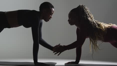 studio shot of two women wearing gym fitness clothing facing each other exercising 2