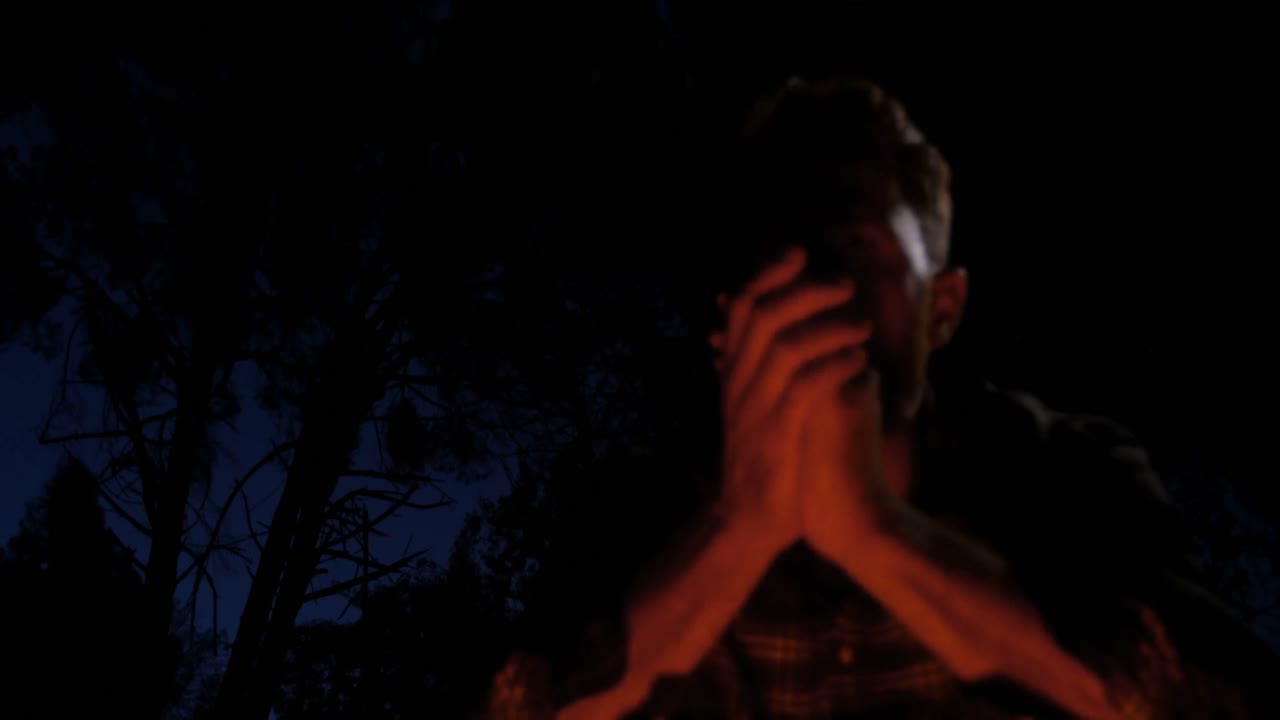 Uomo seduto vicino a un falò nella foresta 4k