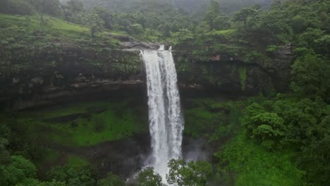 drone view of vasudhara falls in bhandardara, maharashtra, india surrounded by dense forests and lush green mountains, the misty monsoon clouds add a mystical aura to the scenery