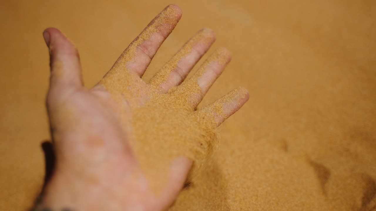 Hand Holds And Lets Fine Golden-brown Sand Flow Through Its Fingers In Merzouga, Morocco. - closeup shot