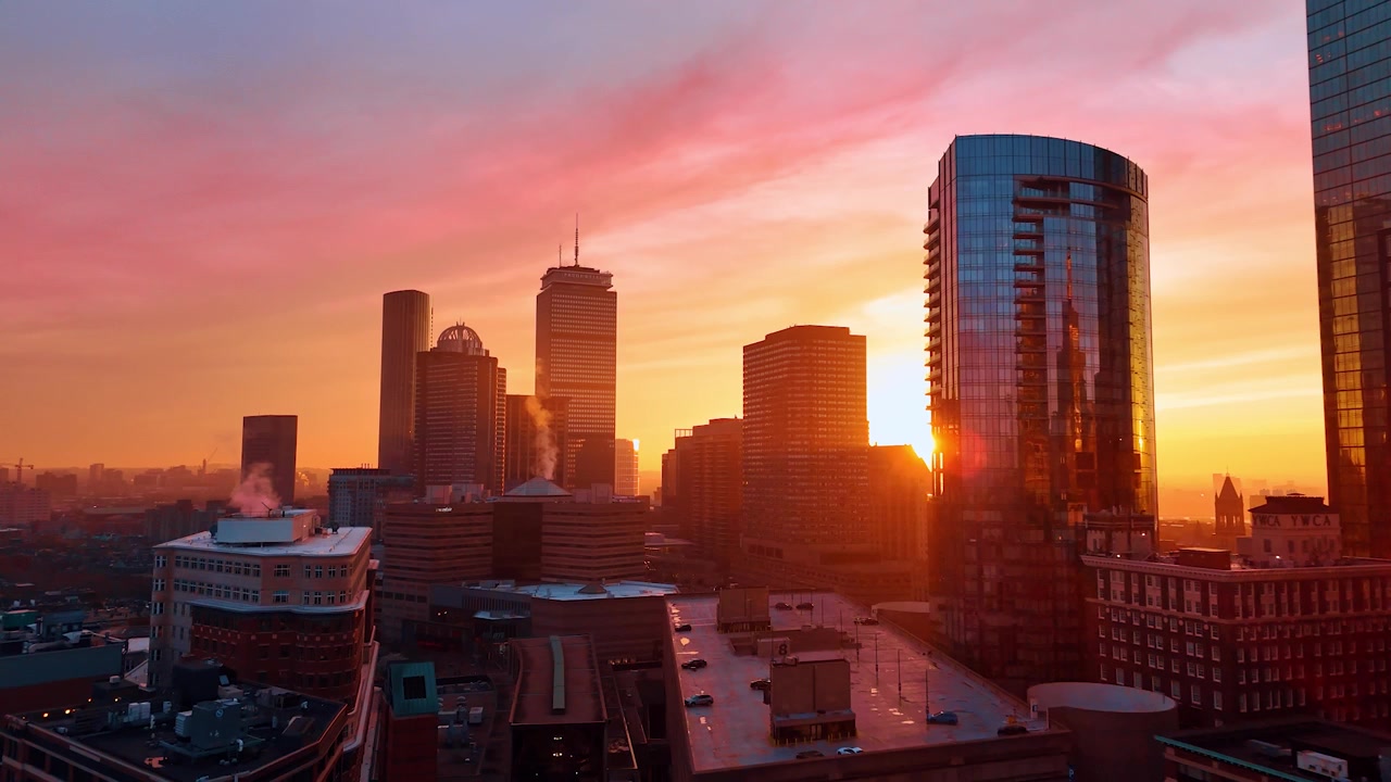 Aproximando-se dos arranha-céus iluminados pelo sol laranja brilhante. Filmagem de drone sobre a paisagem urbana de Boston ao pôr do sol