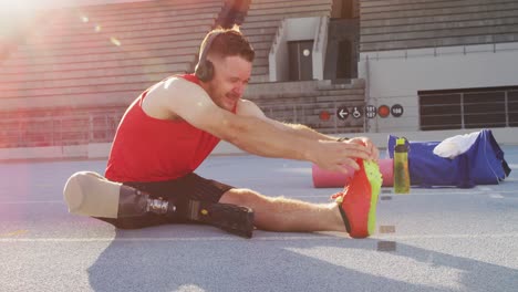 Caucasian-disabled-male-athlete-with-running-blade-wearing-headphones-and-stretching