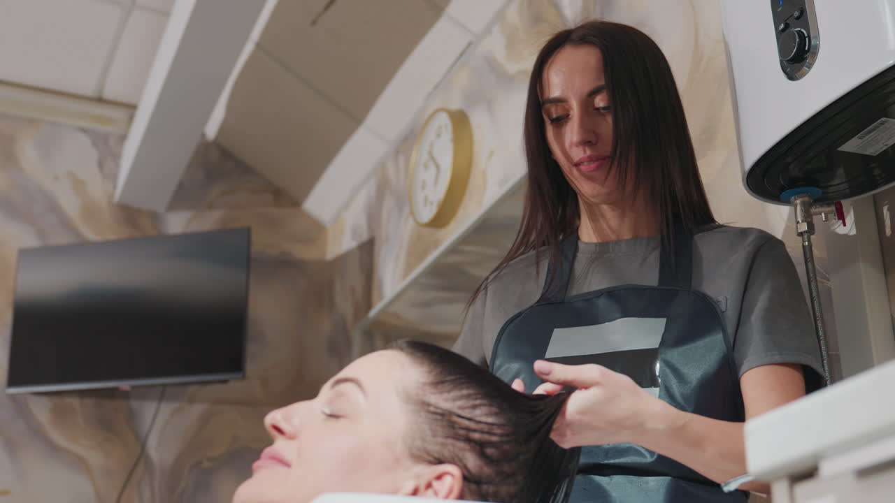 Afslappende hårvask i salonen, fredfyldt hårplejescene med opmærksom stylist og flydende lokker, rolig salonatmosfære, hvor en kaukasisk stylist omhyggeligt renser og plejer vådt hår