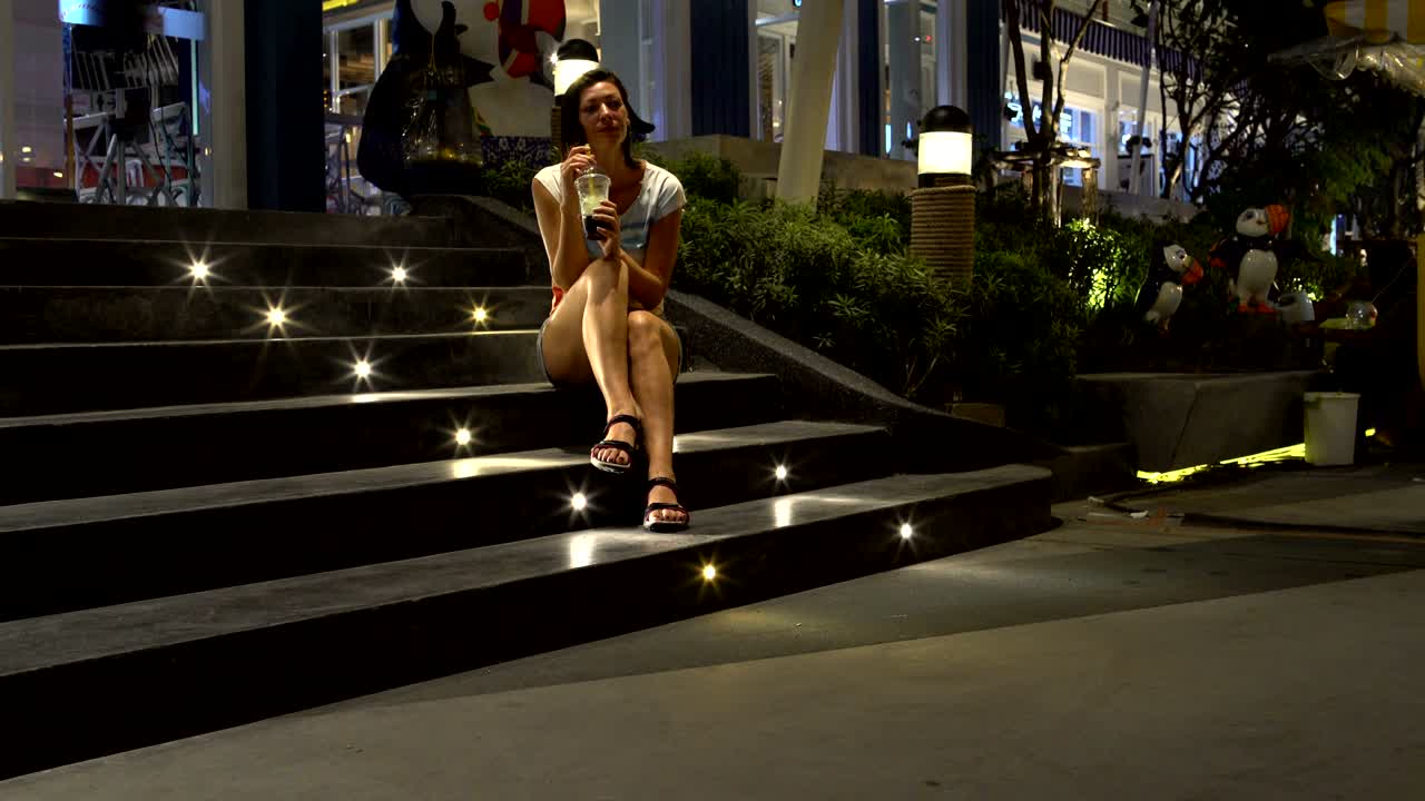 una mujer está sentada en los escalones de un centro comercial y bebiendo té de burbujas