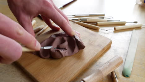 An-artist-sculpting-a-project-with-soft,-brown-modeling-clay-and-hand-tools-on-a-messy-art-studio-table