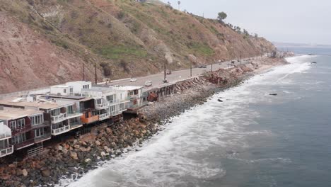 Aerial low close-up shot of surviving beachfront homes alongside cleared lots on Pacific Coast Highway in the aftermath of the Palisades Fire in Malibu, California. 4K