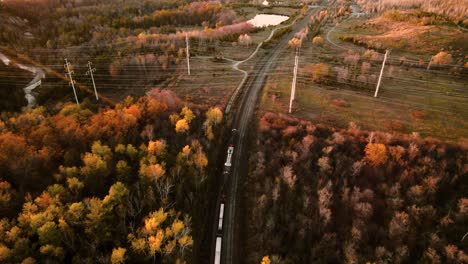 Inclinación-De-Cámara-Lenta-Rastreando-Un-Tren-De-Carga-Que-Viaja-A-Través-De-Un-Vibrante-Paisaje-Otoñal,-Vista-Aérea,-Canadá