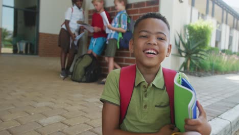 video of happy african american boy holding books in front of school