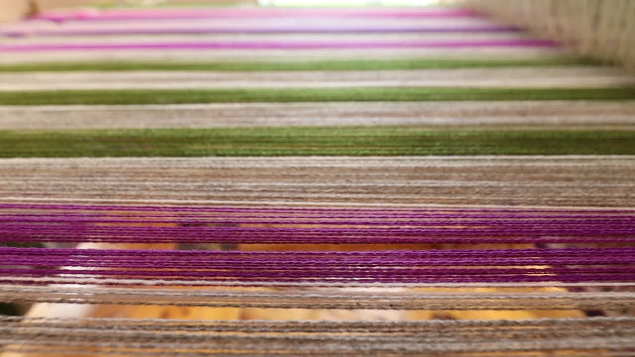 Close-up view of multicolored threads stretched across a traditional hand loom, with natural light coming through the window in the background