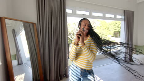 african american young woman wearing striped shirt singing into smartphone, at home, copy space