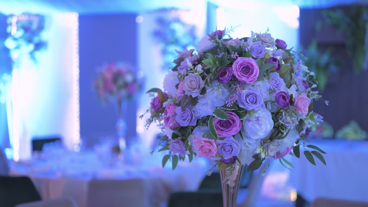 A close-up of an elegant floral centerpiece featuring pastel roses, peonies, and greenery on a tall vase inside a beautifully decorated event hall