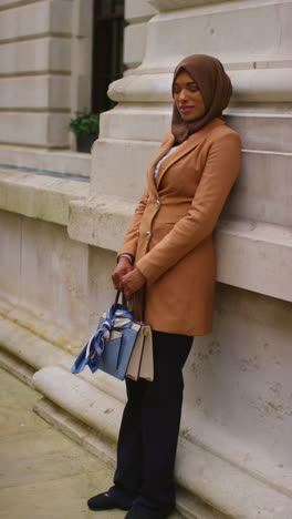 vertical video full length portrait of muslim businesswoman wearing hijab and modern business suit standing outside city office buildings 1