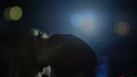 female singer leaning forward on music stage, showing animated lens flares above metal trussing