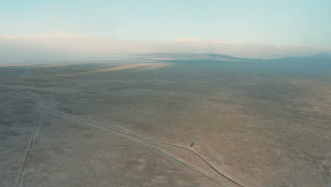 Aerial-orbiting-lone-vehicle-parked-in-vast-high-desert-plain