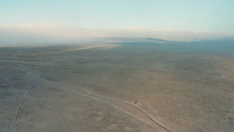 aerial orbiting lone vehicle parked in vast high desert plain