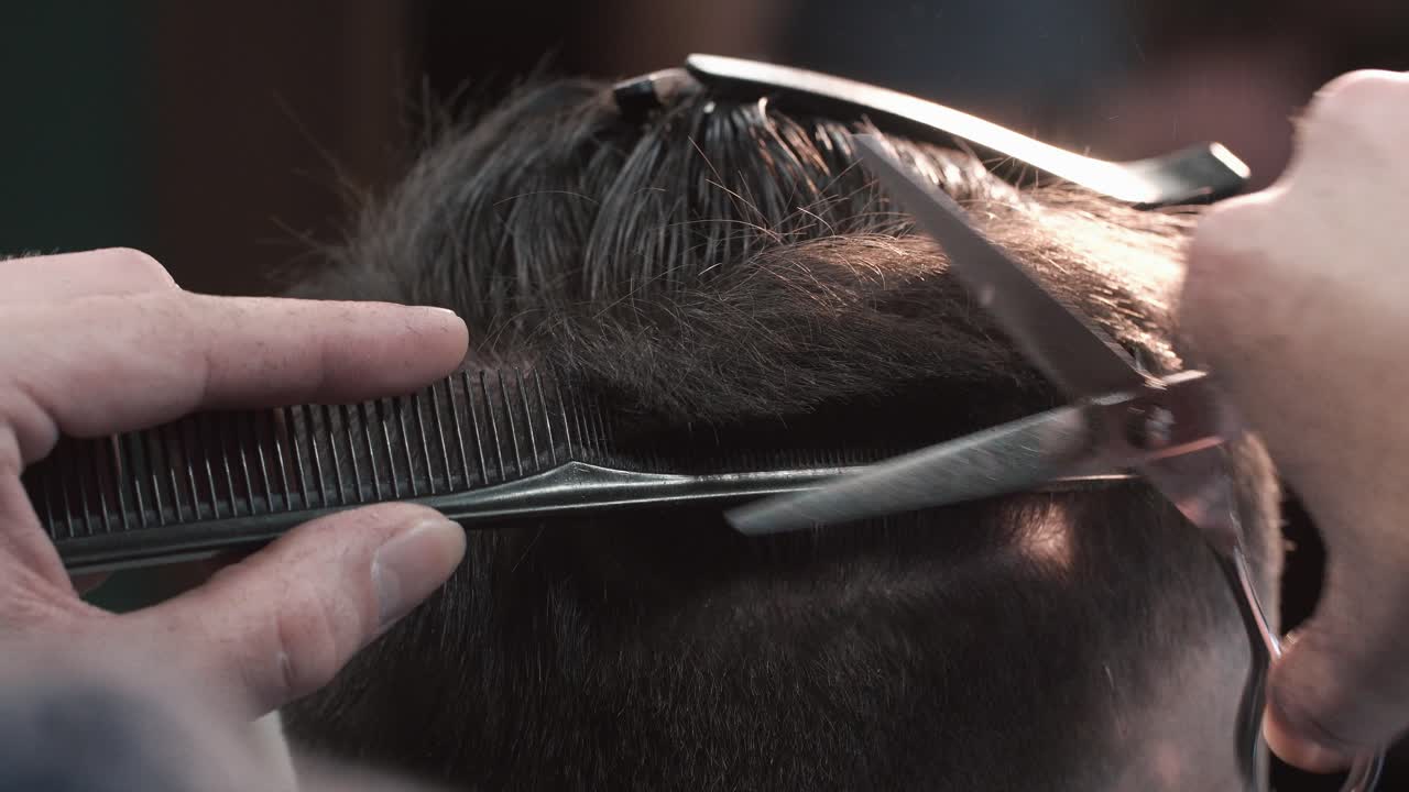 Close-up of a professional barber giving a haircut with comb and scissors