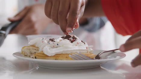 close up of grandson adding sprinkles to pancakes he has made with grandfather in kitchen