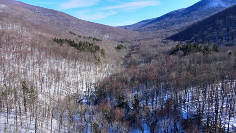 aerial drone footage of a snowy mountain valley in early spring on a sunny day in the appalachian mountain range, just after winter ends with forests and snow and sunshine and blue skies