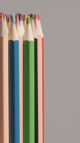 vertical video studio shot of rotating multi-coloured pencils against grey background