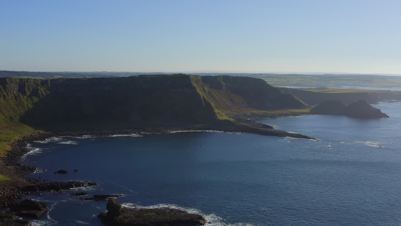 Aerial pan over the Amphitheatre and Giant's Causeway, showcasing a stunning coastal view under a sunny evening sky.