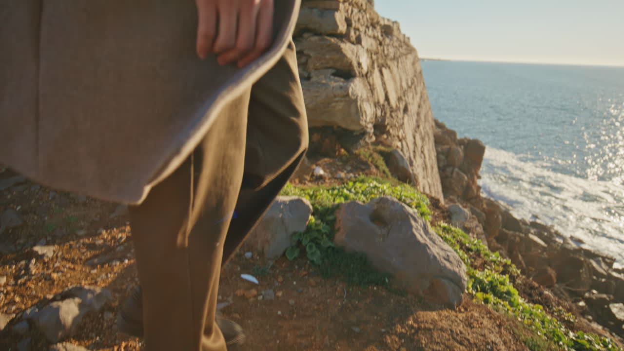 Closeup man legs walking rocky hill. Pensive tourist contemplating ocean nature