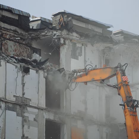 a scoop of demolishing machine breaks off the floors of the destroyed house. excavator working in the cloud of dust