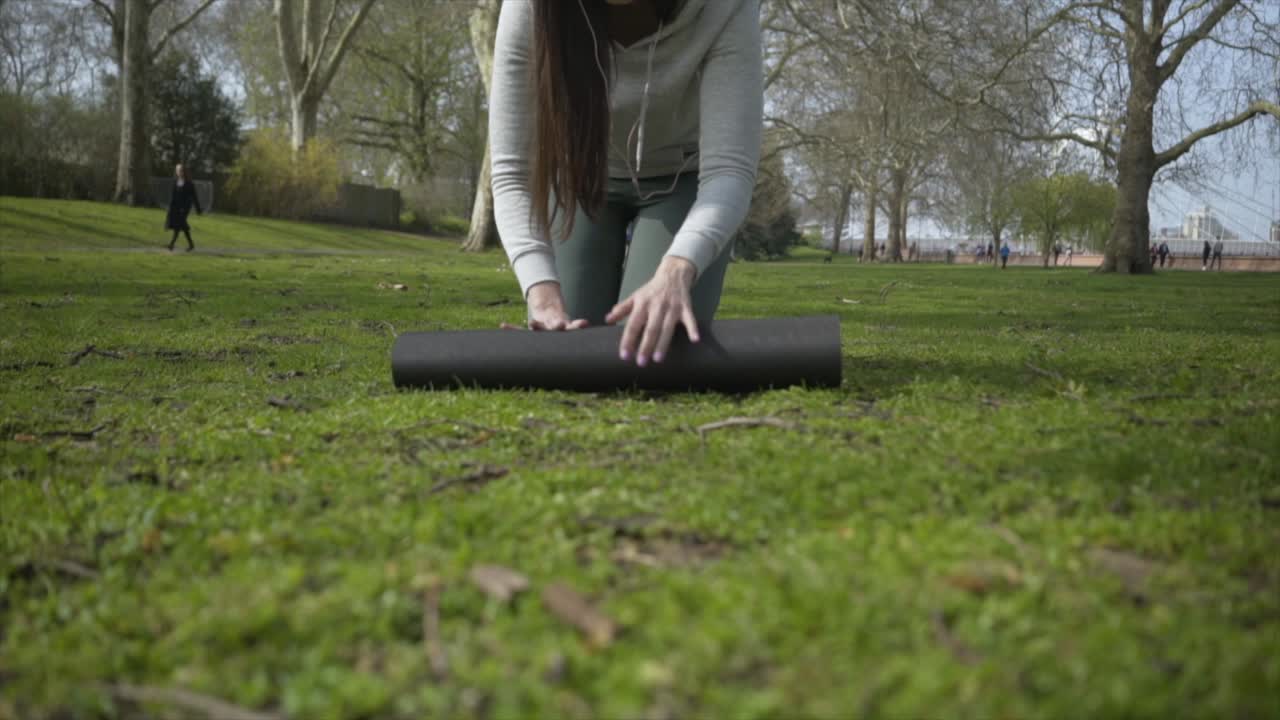 mujer caucásica desplegando su estera de yoga en un parque
