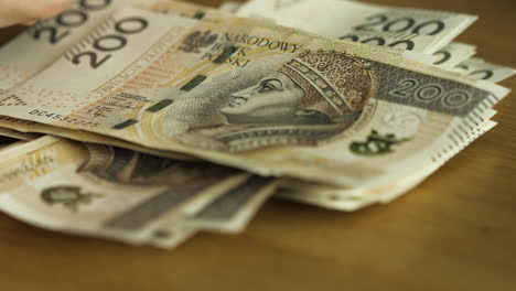 Female-hands-counting-200-Polish-zloty-bills-at-the-table-tight-close-up-shot