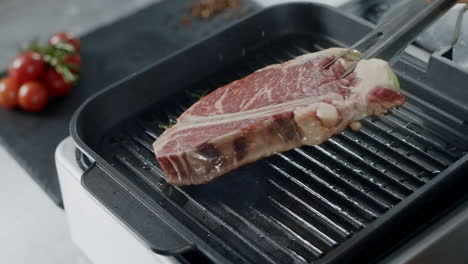 Chef-preparing-meat-at-griddle.-Closeup-man-hands-turning-steak-with-tongs.