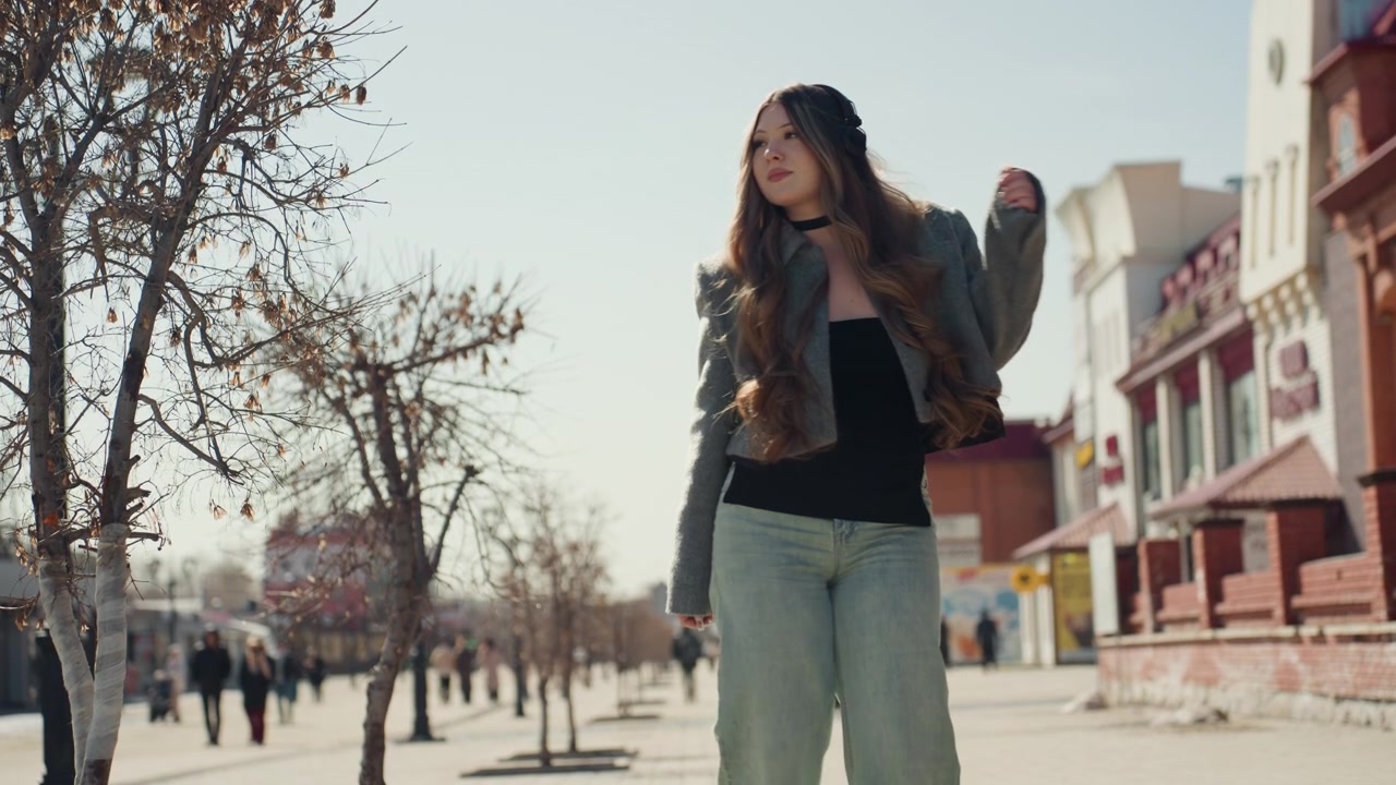 Signora alla moda cammina all'aperto. Elegante modella si muove con sicurezza lungo un viale urbano illuminato dal sole. Donna asiatica attenta alla moda cammina con grazia tra i vivaci dintorni della città in una giornata luminosa