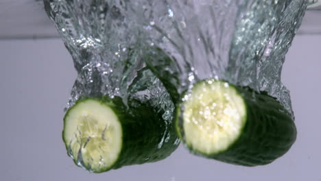 courgette halves falling in water on white background