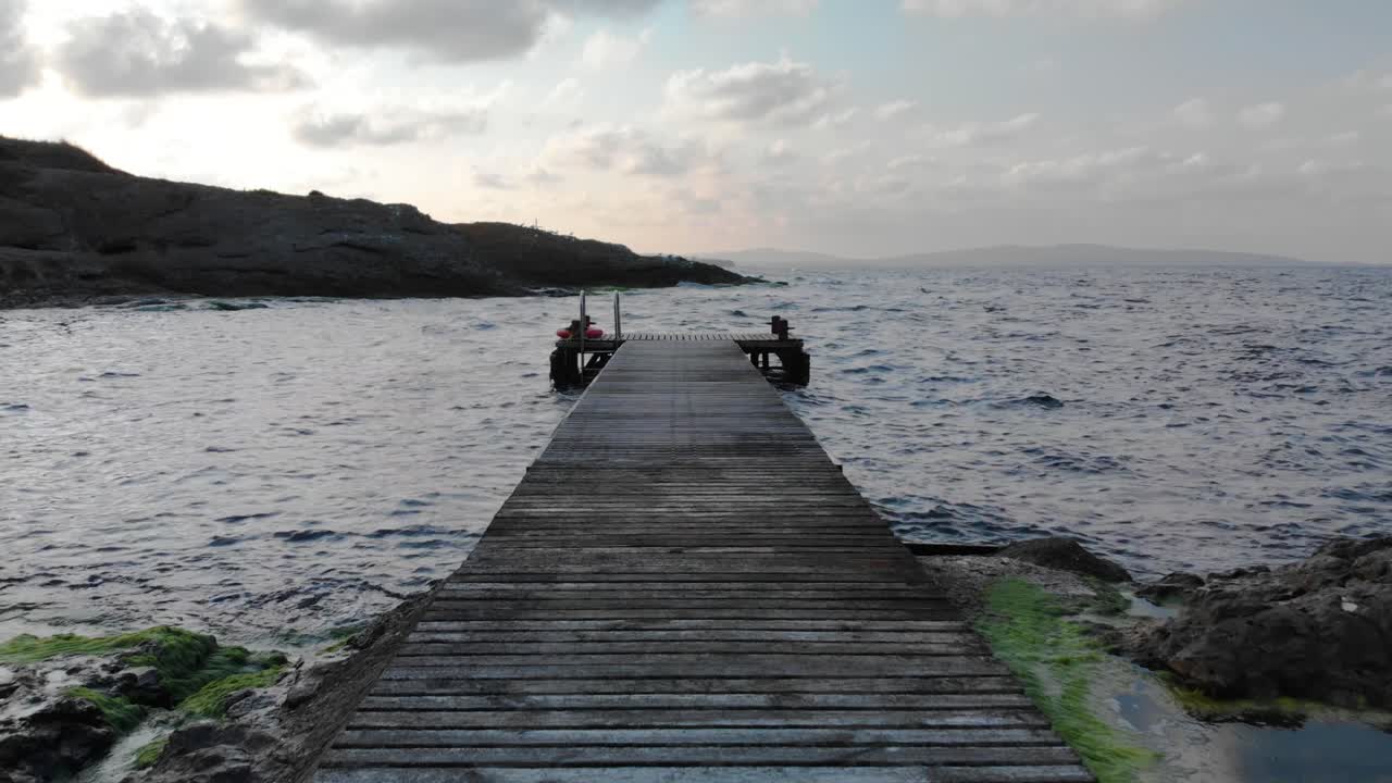 el tiro se mueve hacia abajo y horizontalmente a lo largo del muelle de madera desde la orilla hasta el mar al atardecer