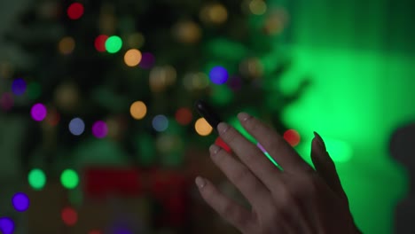 female hands touching the screen of a mobile phone close-up at night, girl shows green screen on a smartphone on the background of christmas tree
