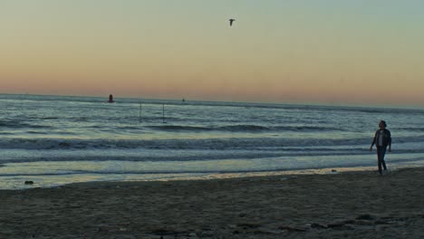 Kaukasisches-Männliches-Mannmodell-Spaziert-Am-Strand-In-Der-Nähe-Des-Meeresozeans-Am-Sandstrand-Mit-Sonnenuntergang-Und-Filmischer-Aufführung