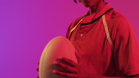 african american female rugby player with rugby ball over neon pink lighting