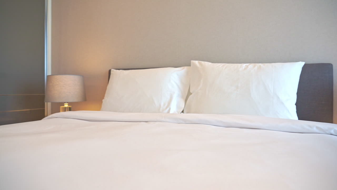 роскошный номер в гостинице бангкока с застеленной белым бельем кроватью королевского размера и ночными светильниками по бокам, дневное время слева