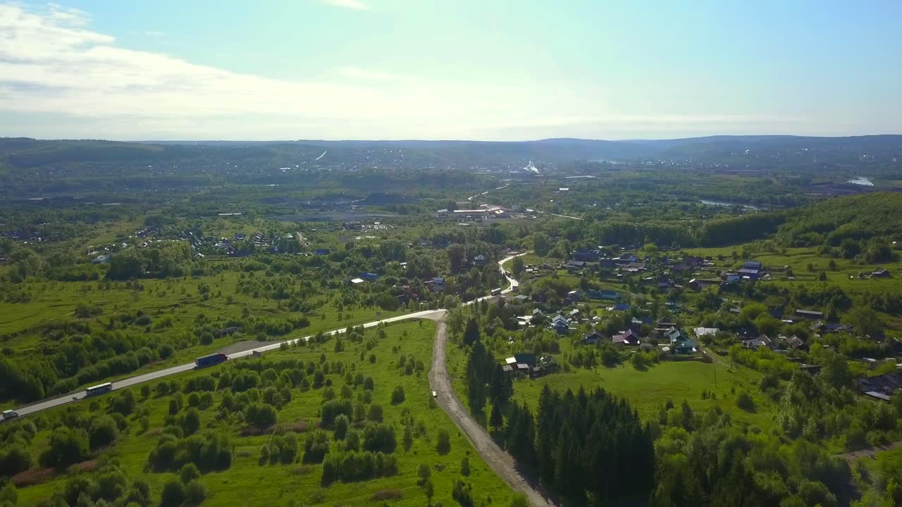 воздушный вид на сельскую деревню, расположенную в долине с шоссе и окружающей зеленью.
