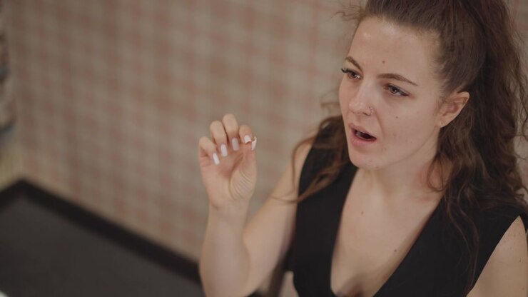 Studente di canto che pratica l'intonazione con un gesto della mano in un'aula di musica, bocca aperta che modella le vocali, occhi concentrati, atmosfera di prova informale con coaching e attenzione tecnica