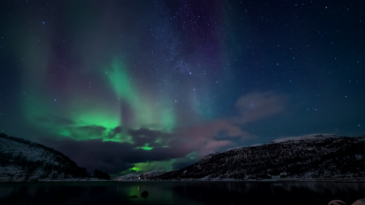 Aurora borealis dancing over Skarsfjord, Norway, snow-covered landscape and starry night sky reflecting on calm waters. Perfect for travel and nature themes. Time-lapse, copy-space