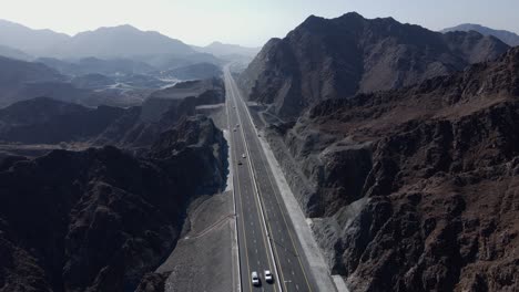 Rear-drone-view-of-UAE-Mountain-range,-Traffic-movement-in-between-the-Khorfakkan-mountains,-Sharjah,-United-Arab-Emirates