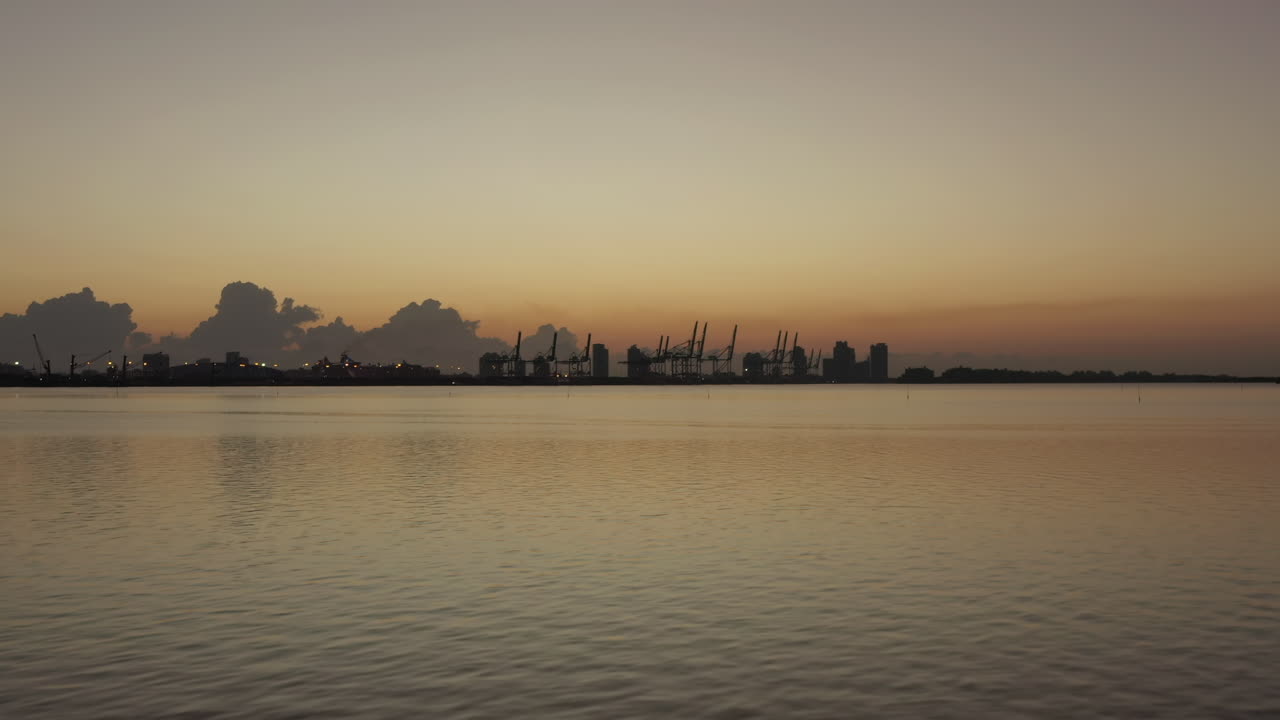 일몰 시 마이애미 해안선에 실루엣 타이드 마커가 있는 선적항 크레인을 향해 이동하는 공중 전망